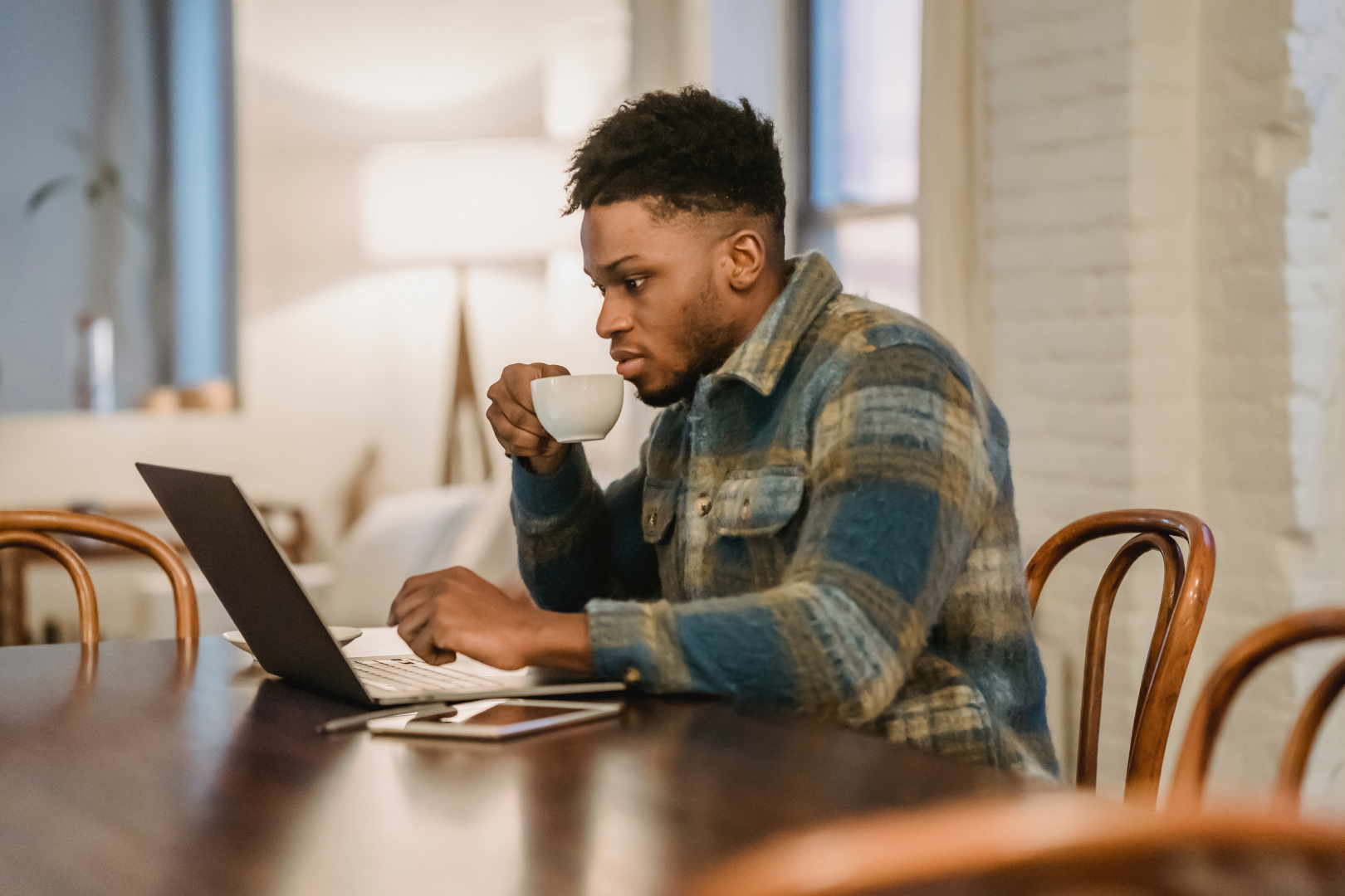 young man at table, drinking coffee and using a laptop