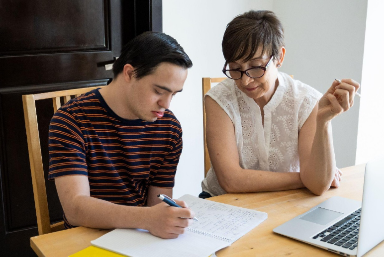 A teen writing in a journal, sitting next to an adult