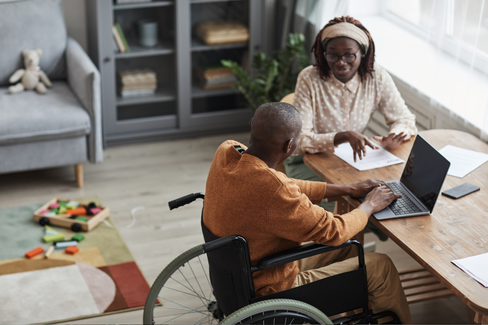 A man using a wheelchair and woman sitting at a table talking.