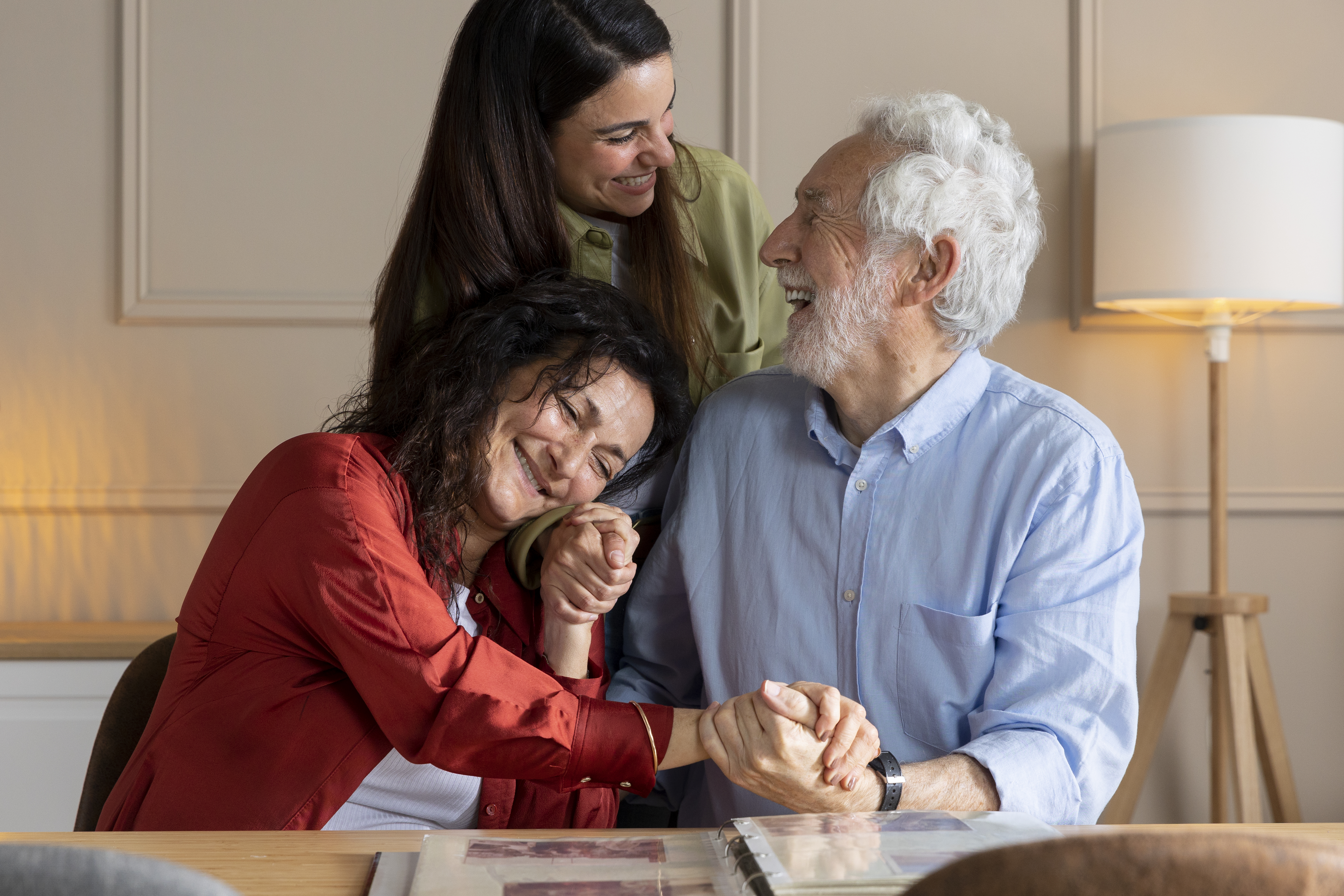 Two women and a senior man smiling, looking at a photo album