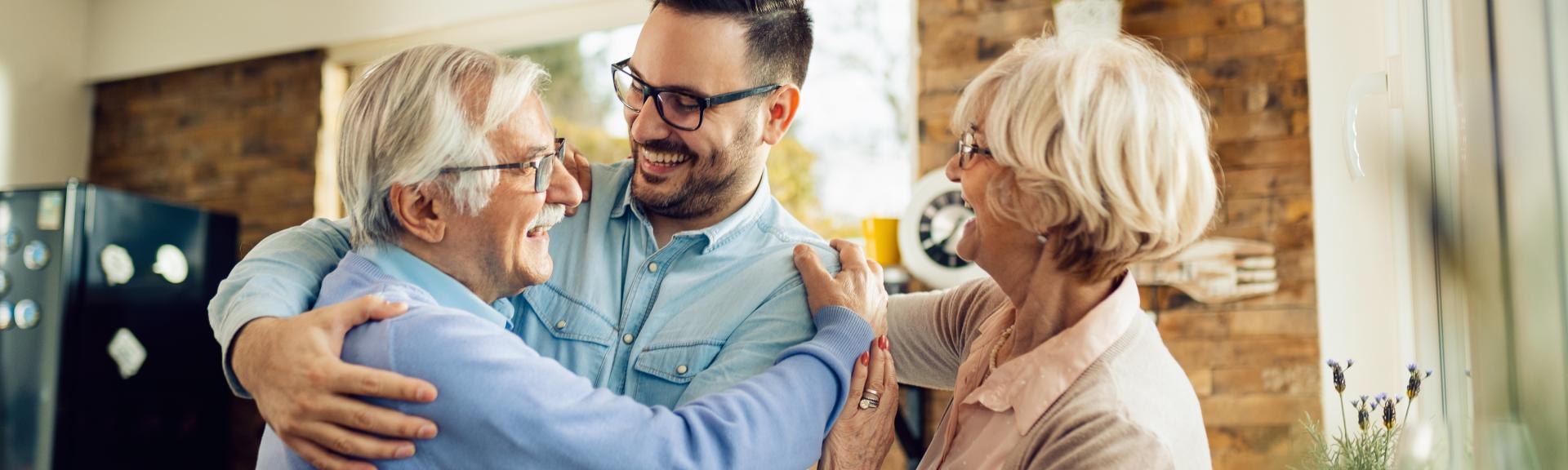 two seniors and a younger adult hugging and smiling