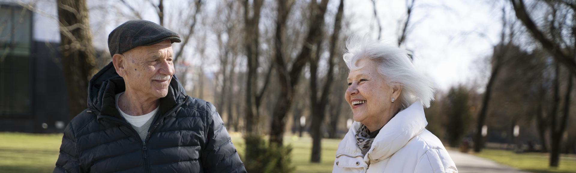 two senior adults outside, smiling at each other
