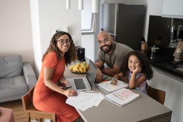Family at table with laptop doing homework looking at the camera smiling