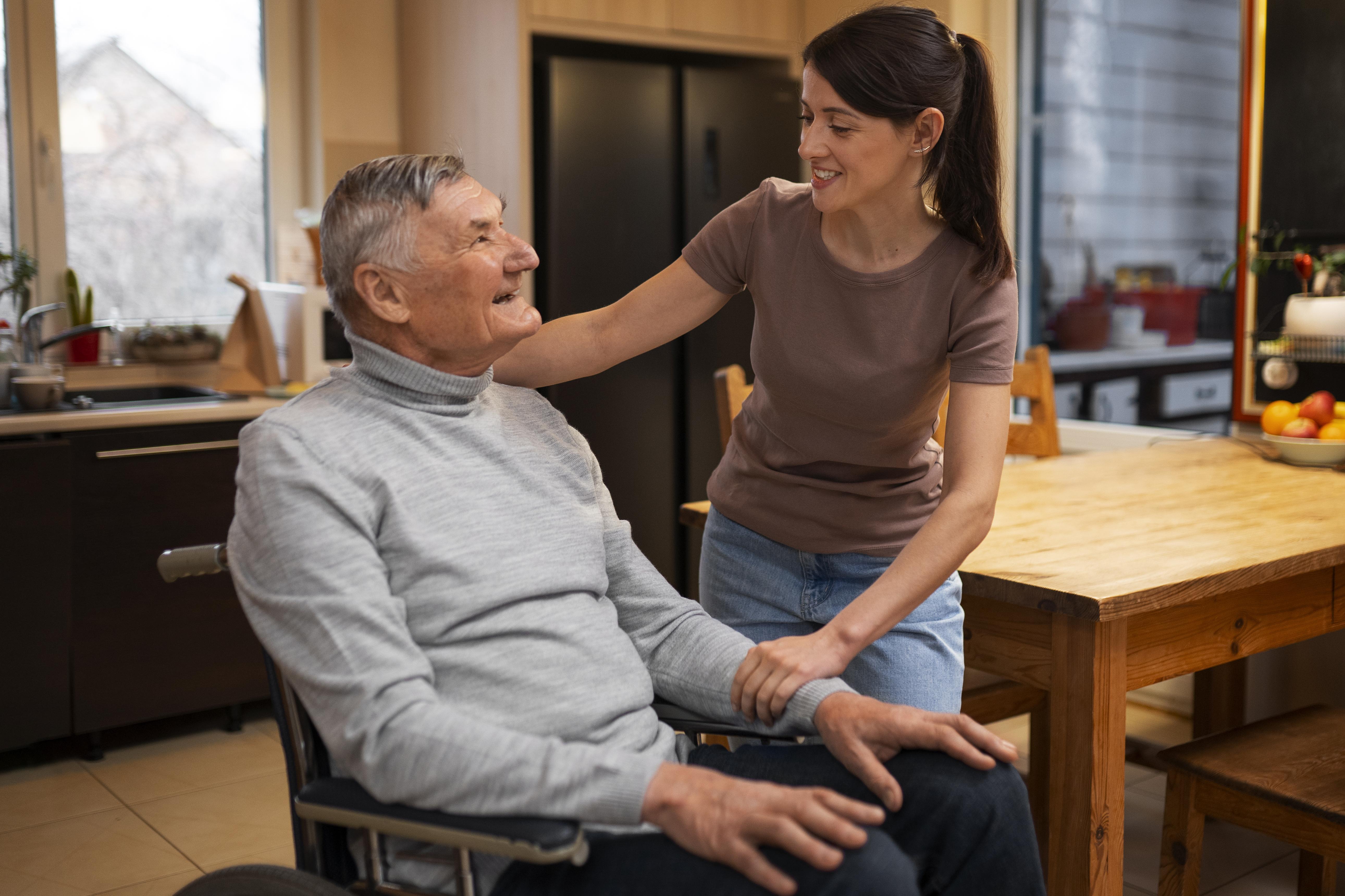 Elderly man using wheelchair and smiling with female caregiver